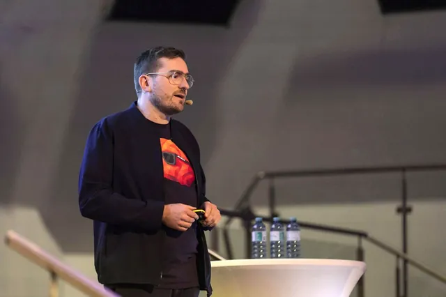 Christian Dietz spricht beim OMT 2026 auf der Bühne, im T-Shirt mit dem roten Low-Poly-Gehirn FRED