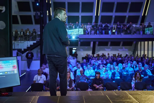 Christian Dietz bei seiner Neuromarketing-Keynote auf dem OMT 2026, vor ihm der volle Saal mit Empore