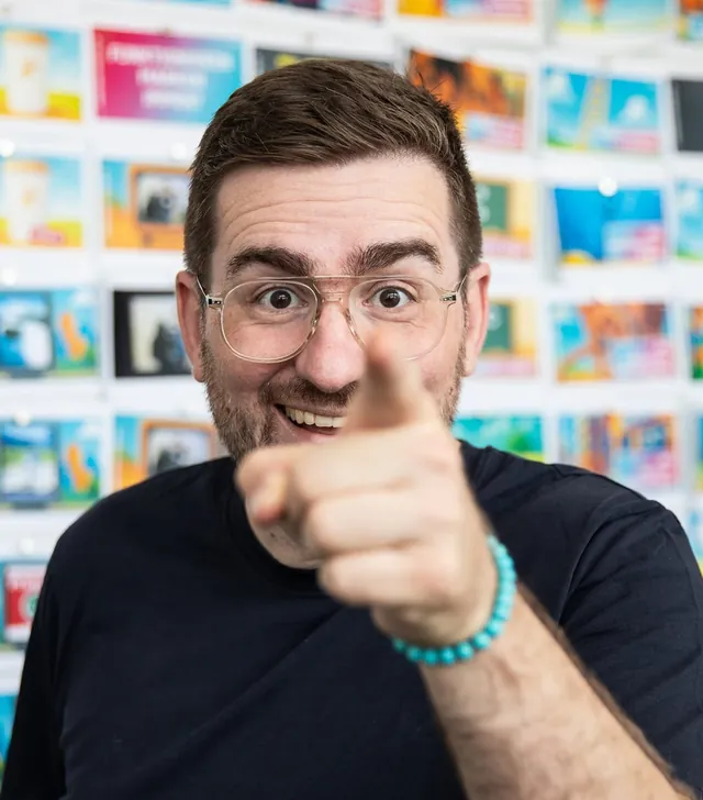 Christian Dietz zeigt lachend mit dem Finger in die Kamera, hinter ihm eine Wand voller bunter Folien