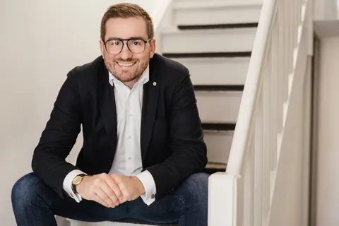 Christian Dietz sitting on a white wooden staircase, smiling