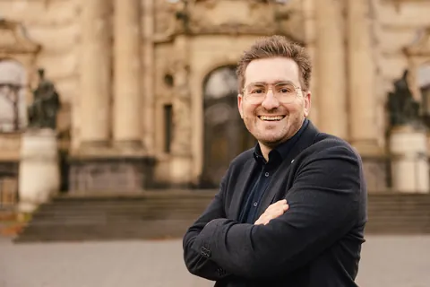 Christian Dietz with arms crossed in front of a historic building