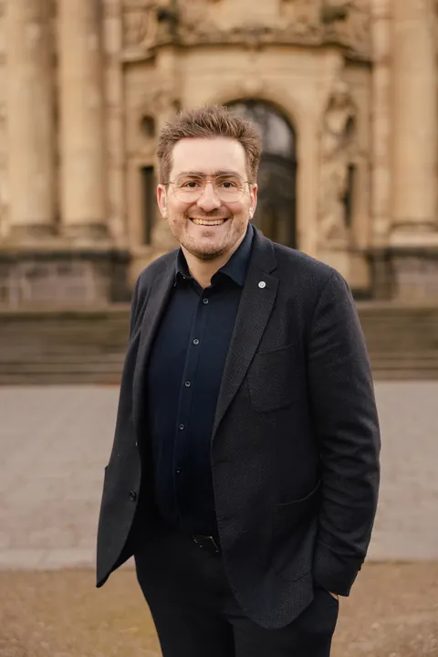 Christian Dietz with his hands in his pockets in front of a historic doorway