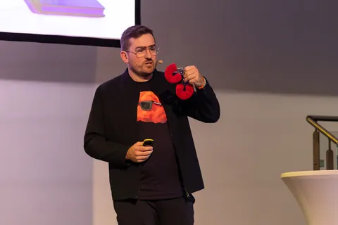 Christian Dietz in the FRED shirt on stage, holding up a red object