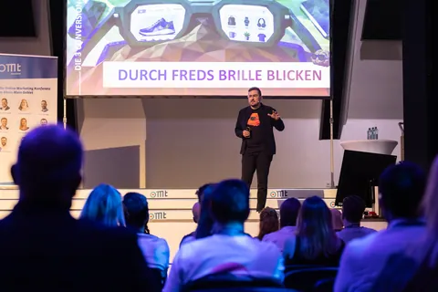 Christian Dietz on stage at OMT 2026 in Mainz in front of a slide about looking through FRED’s glasses, the audience in the foreground