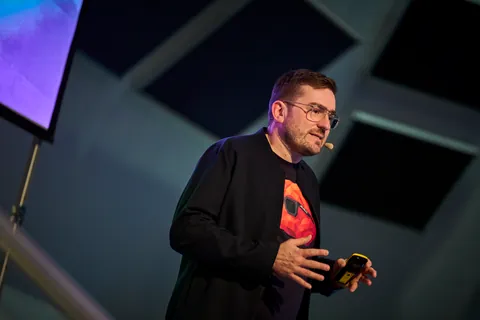 Close-up of Christian Dietz on stage at OMT 2026 in Mainz, with headset and clicker, black jacket over the FRED shirt